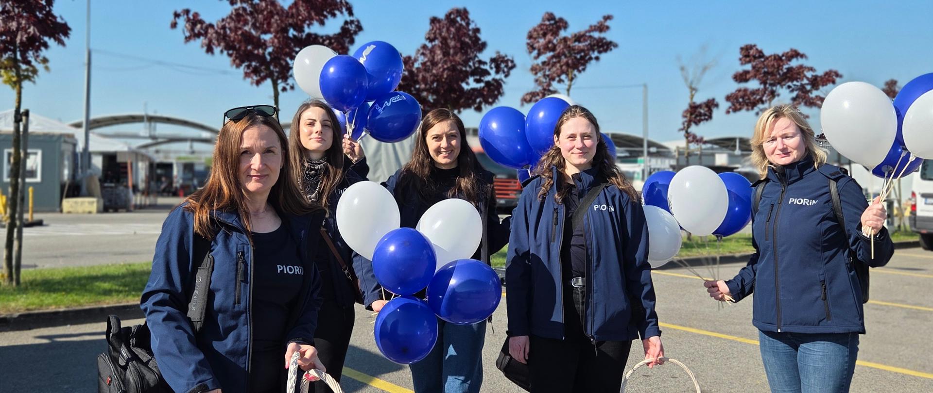 Cztery kobiety w granatowych bluzach stoją z balonami i koszykami 