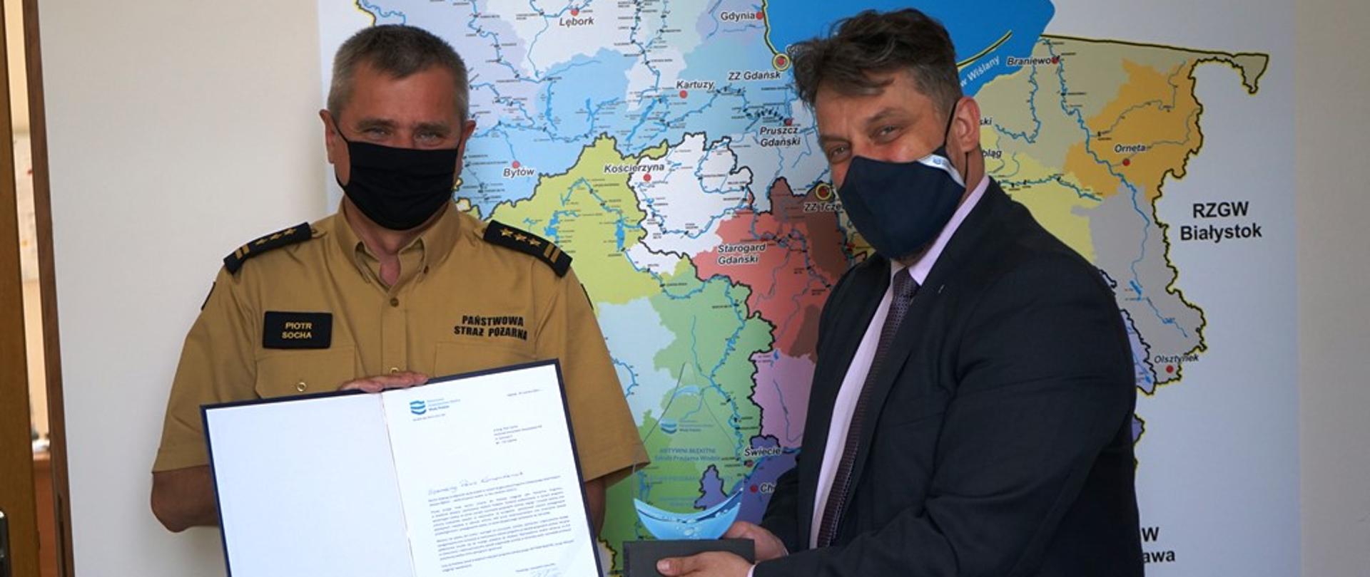 Pomorski komendant wojewódzki Państwowej Straży Pożarnej trzyma podziękowanie a dyrektor wręcza statuetkę partnera programu "Aktywni Błękitni".