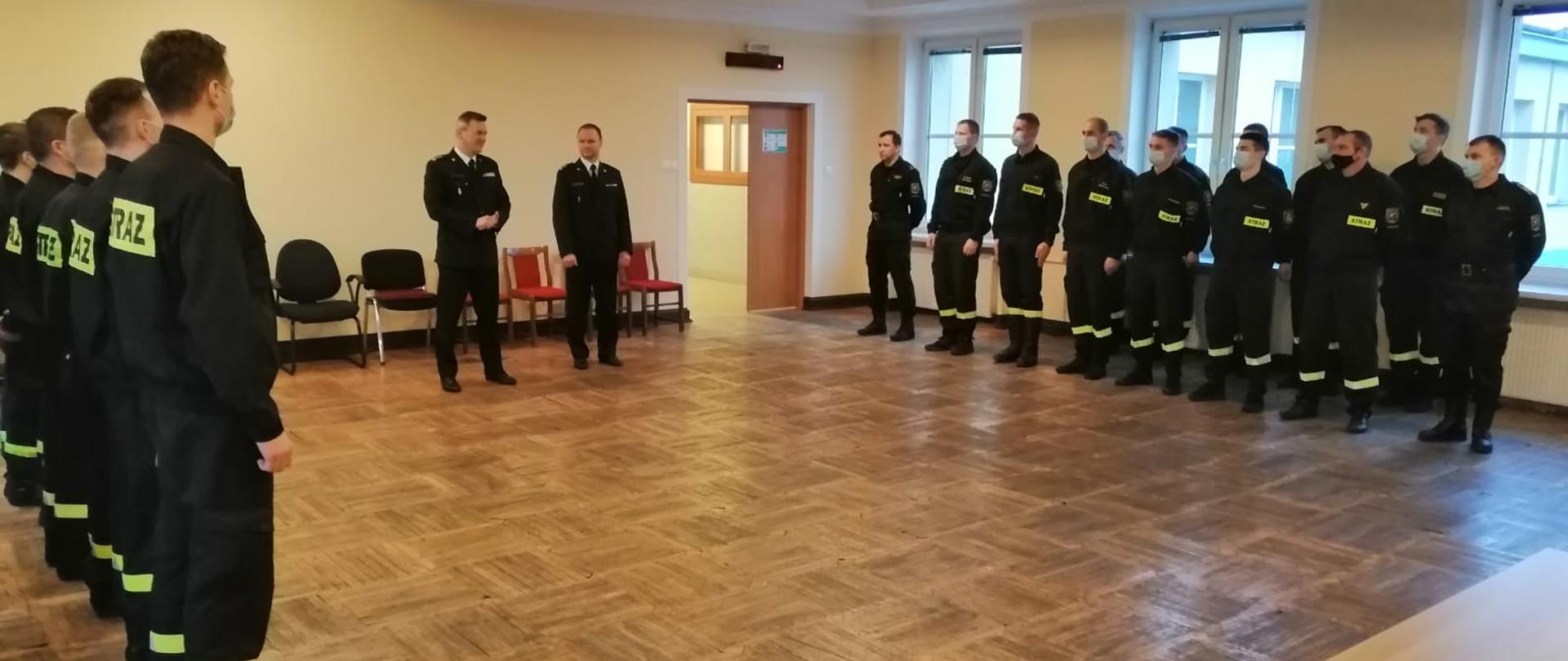 Strażacy w dwóch rzędach stoją na sali w JRG 7 przed Komendantem Miejskim PSP m.st. Warszawy i Dowódcą Jednostki