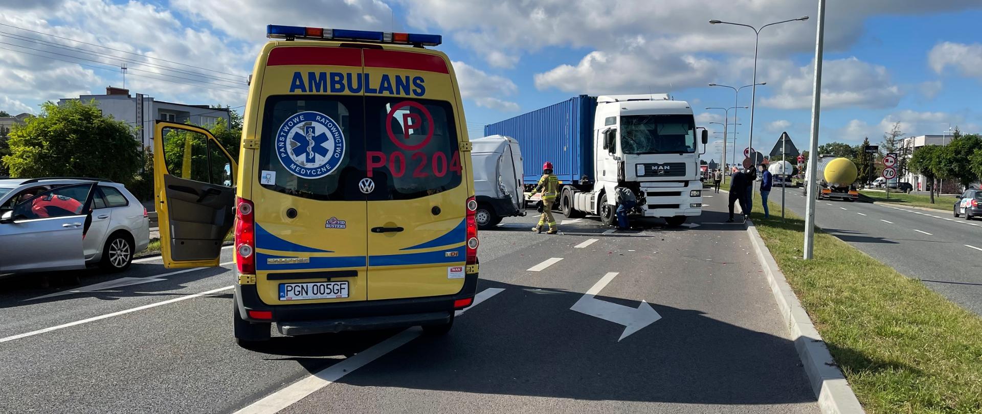 Na zdjęciu widać karetkę pogotowia. Po lewej stronie karetki znajduje się samochód osobowy biorący udział w zdarzeniu. Za karetką widać jeszcze busa oraz TIRa, który również brały udział w kolizji. Samochody blokują całkowicie drogę