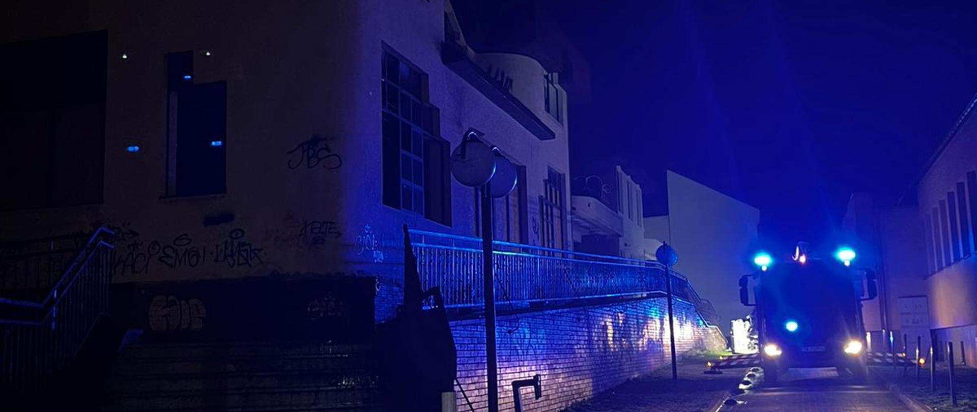 Zdjęcie przedstawia ulicę Silniczną w Kielcach. Po lewej stronie stoi opuszczony budynek gdzie doszło do pożaru, po prawej, na jezdni zaparkował samochód pożarniczy.