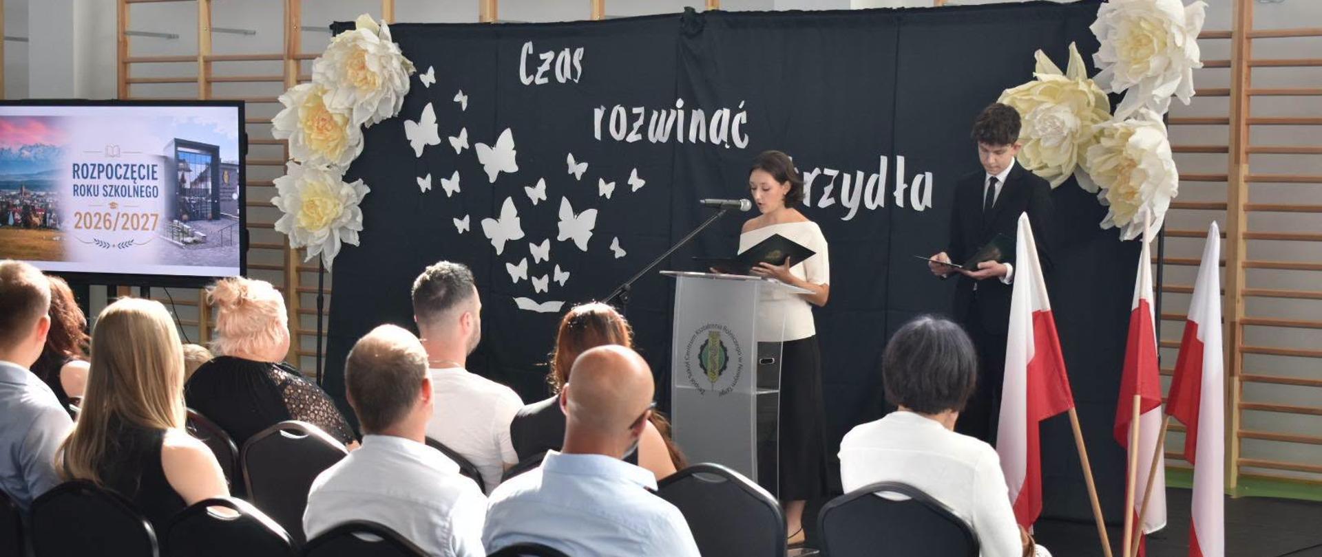 Zdjęcie osób prowadzących akademię z okazji rozpoczęcia roku szkolnego oraz osób siedzących na krzesłach