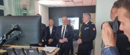 Strażak, zaproszeni goście stoją przed monitorami razem z nimi stoją przedstawiciele prasy.