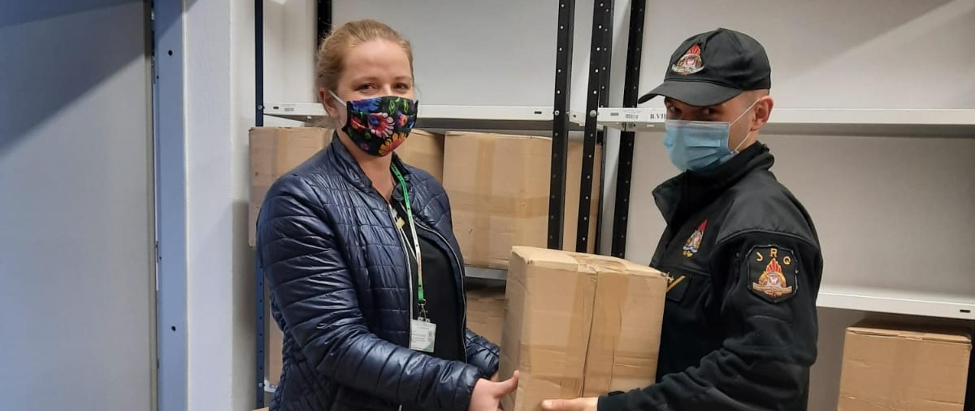 Strażak przekazuje pudełko kartonowe pracownikowi na tle magazynowych regałów