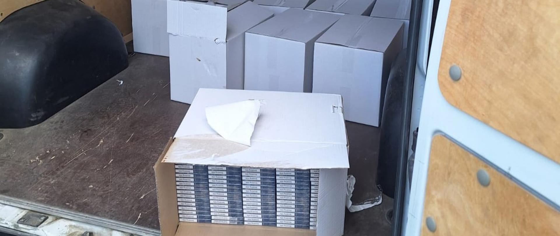 W przestrzeni ładunkowej samochodu dostawczego znajduje się wiele białych kartonów, wewnątrz jednego widać paczki papierosów.