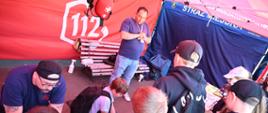 Dzieci uczą się pierwszej pomocy pod okiem instruktorów w namiocie promocyjnym numeru alarmowego 112. Chłopiec ćwiczy uciski klatki piersiowej na fantomie medycznym.