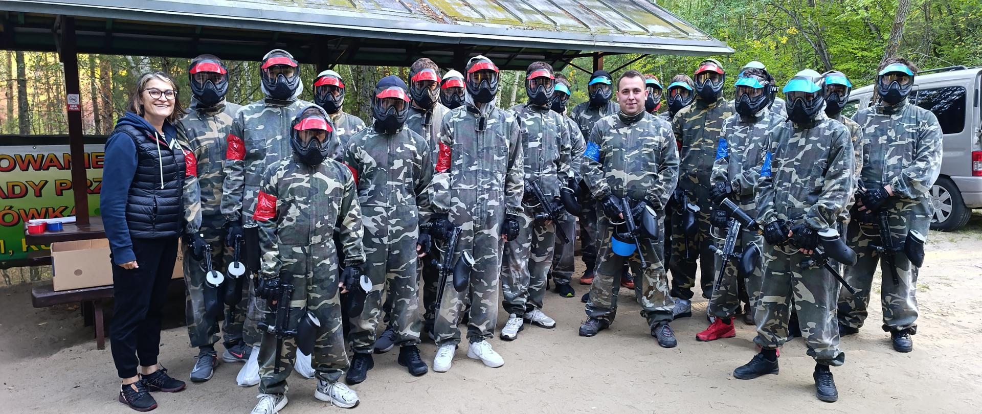 Grupa uczestników przygotowuje się do gry paintballowej w lesie.