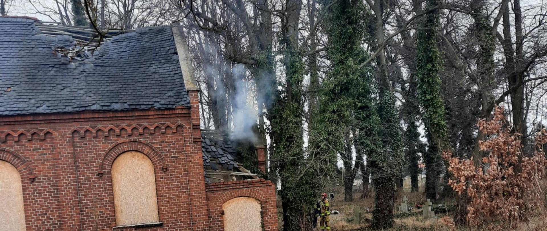 Budynek kaplicy cmentarnej oraz strażacy gaszący pożar.