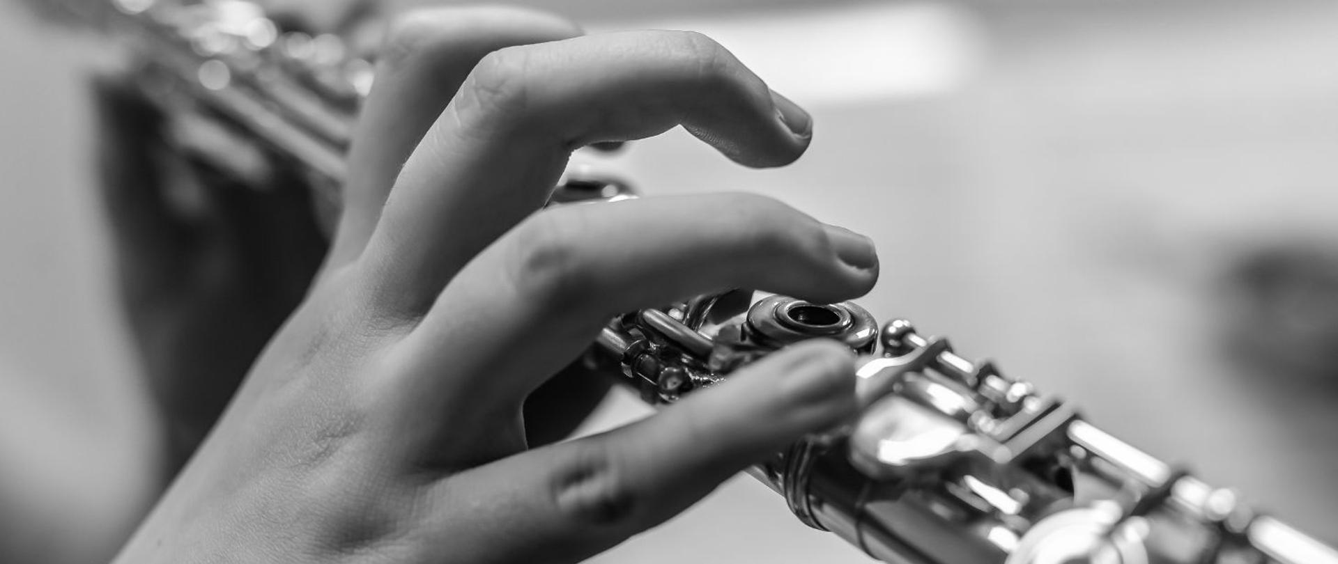 biało-czarne zdjęcie przedstawia ręce flecisty, zbliżenie na detale fletu poprzecznego kadrowanego po skosie