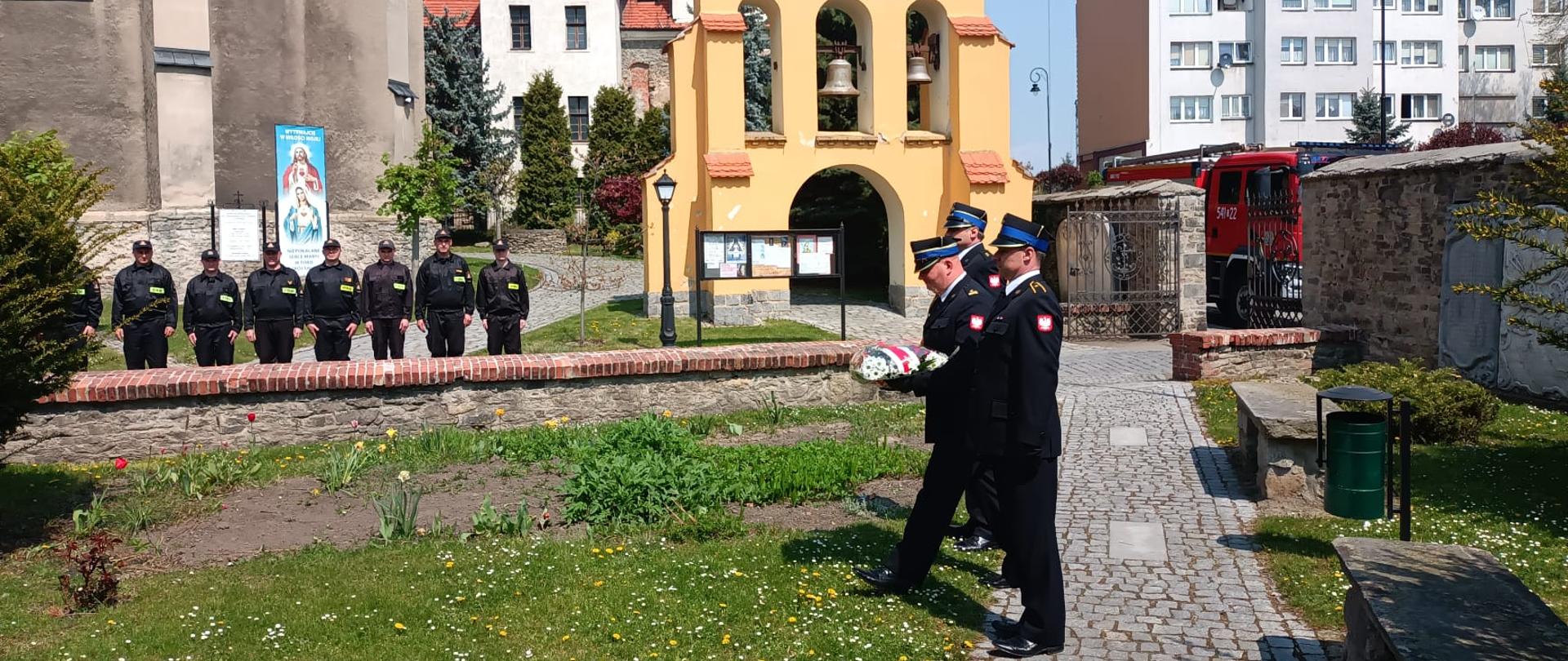 Strażacy składający kwiaty pod pomnikiem