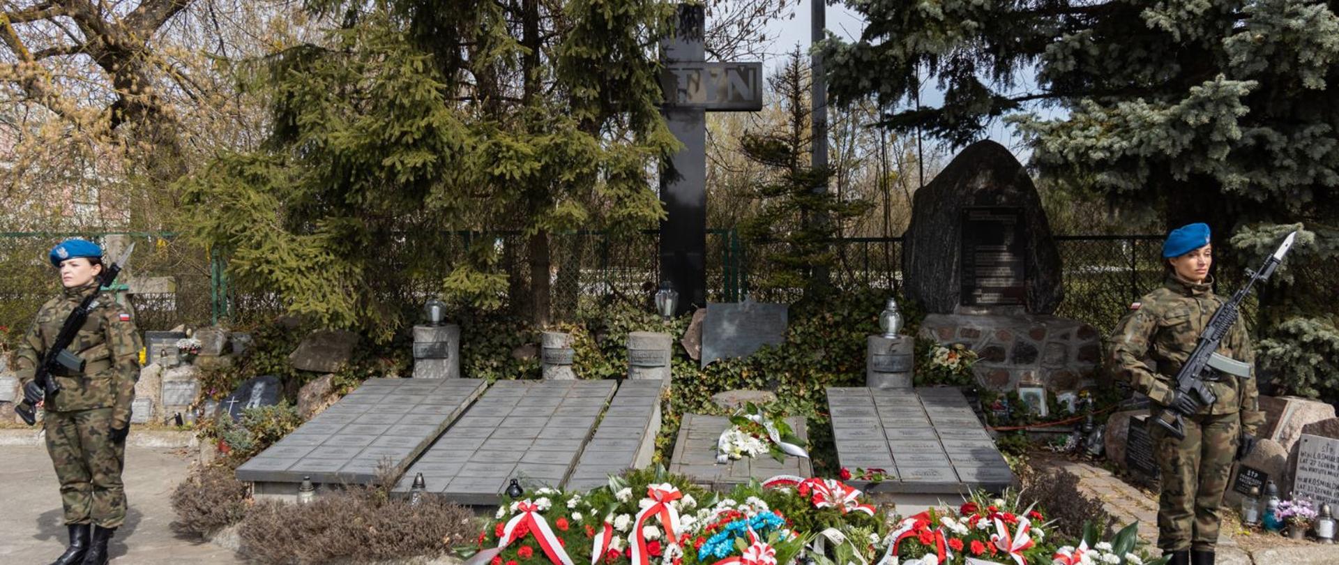 Przy przypominkach, gdzie zostały złożone kwiaty stoją dwie żołnierki w mundurach, które oddają hołd.