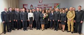 Strażacy oraz pracownicy cywilni stoją w świetlicy Komendy podczas uroczystej zbiórki z okazji przejścia na zaopatrzenie emerytalne oraz mianowania na wyższe stanowiska służbowe
