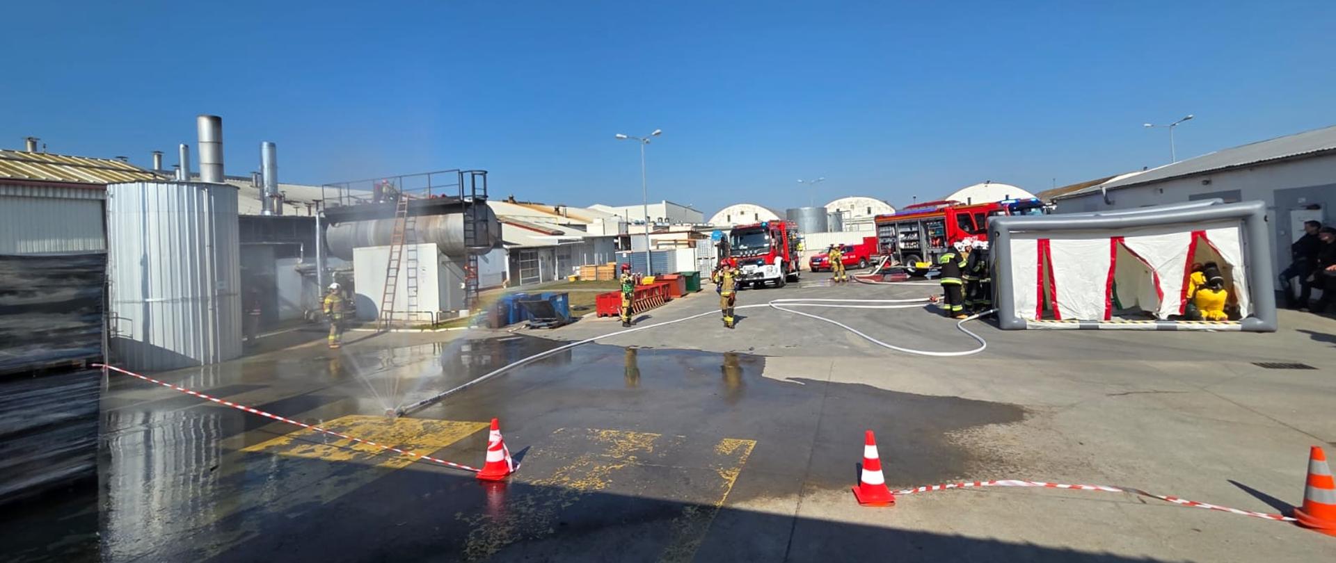 Ćwiczenia w firmie Bonduelle Polska S.A. Zakład Produkcyjny w Ruchocicach. W tle pojazdy pożarnicze, sprawiony sprzęt ratowniczy.