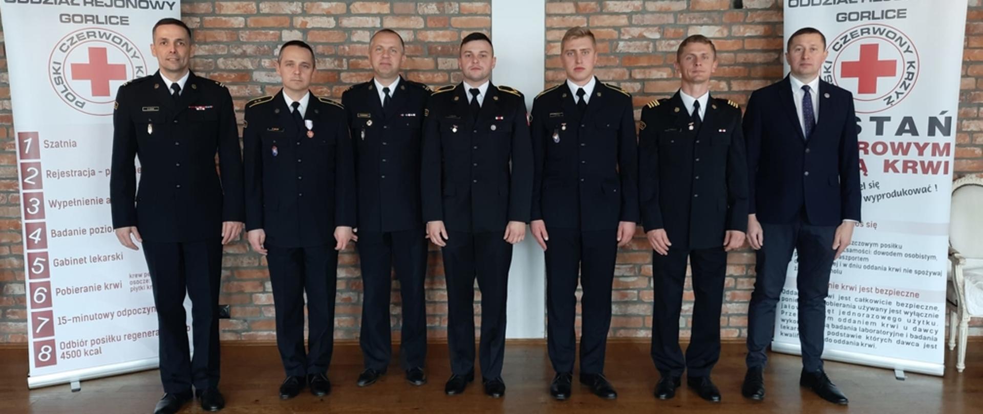 Na zajęciu widoczni wyróżnieni strażacy w mundurach wyjściowych wraz z Komendantem Powiatowym PSP w Gorlicach uczestniczący w Gali Honorowych Dawców Krwiodawców powiatu gorlickiego. 