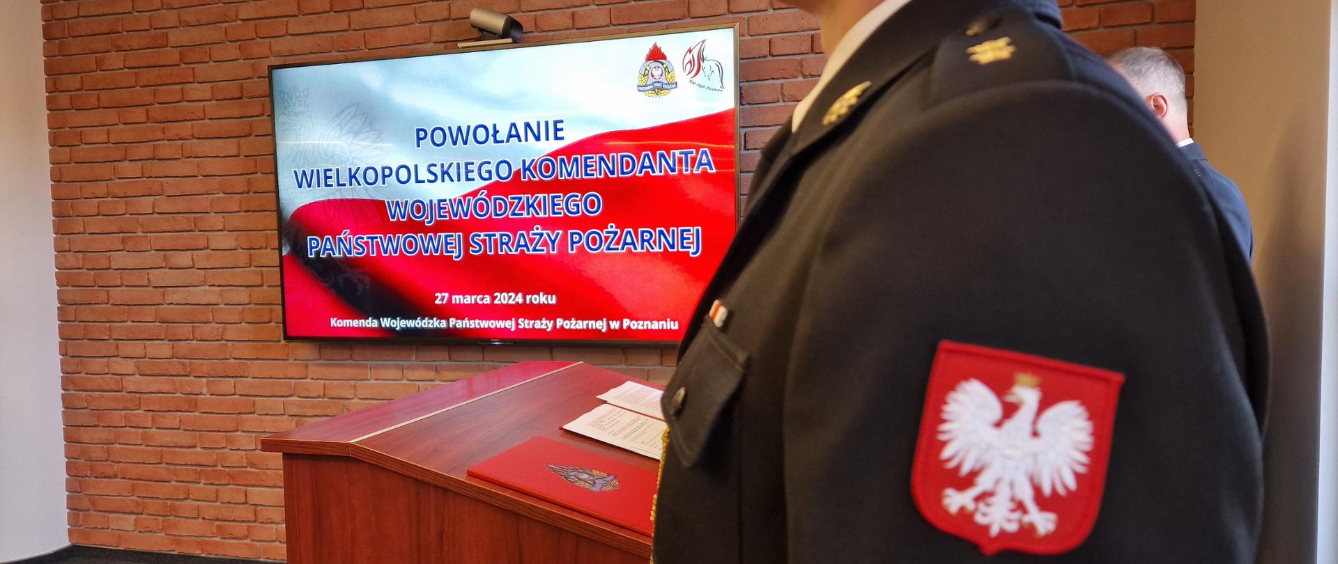 Zdjęcie poglądowe, na pierwszym planie po prawej stronie emblemat z orłem w koronie a w tle ekran telewizora z napisem "Powołanie wielkopolskiego komendanta wojewódzkiego" 