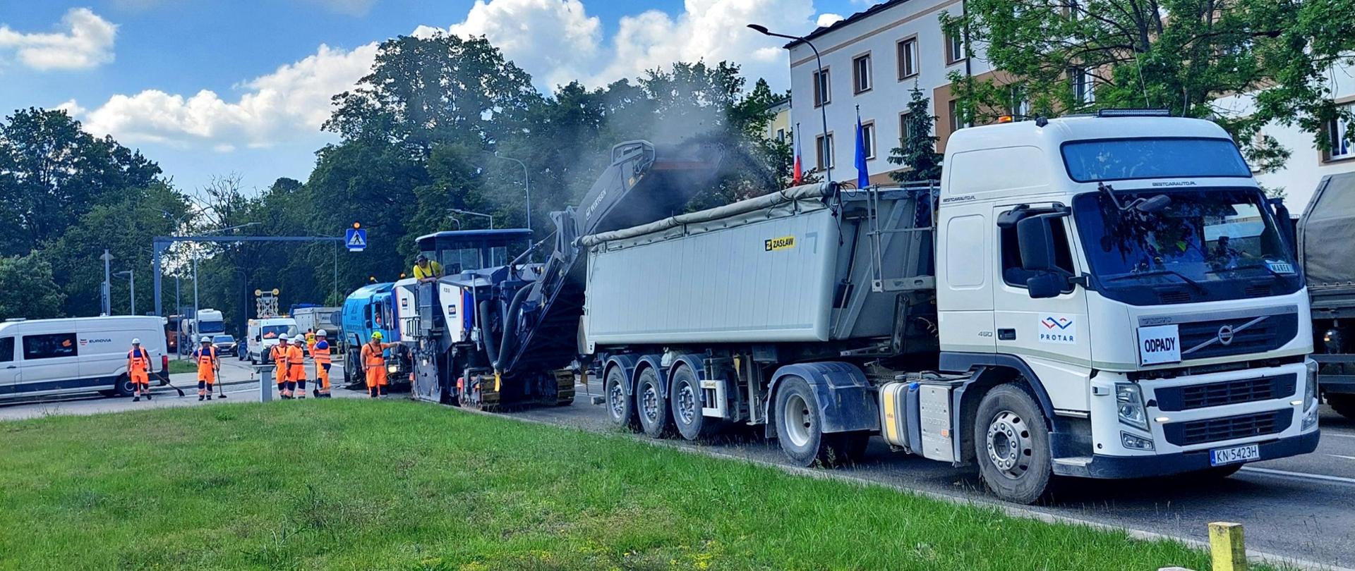 Na zdjęciu widoczny jest samochód ciężarowy i pracownicy remontujący drogę.