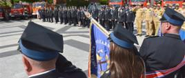Na zdjęciu widać strażaków stojących na placu podczas przeglądu pododdziału. Na pierwszym planie widać prezentację sztandaru przez jedno z OSP.