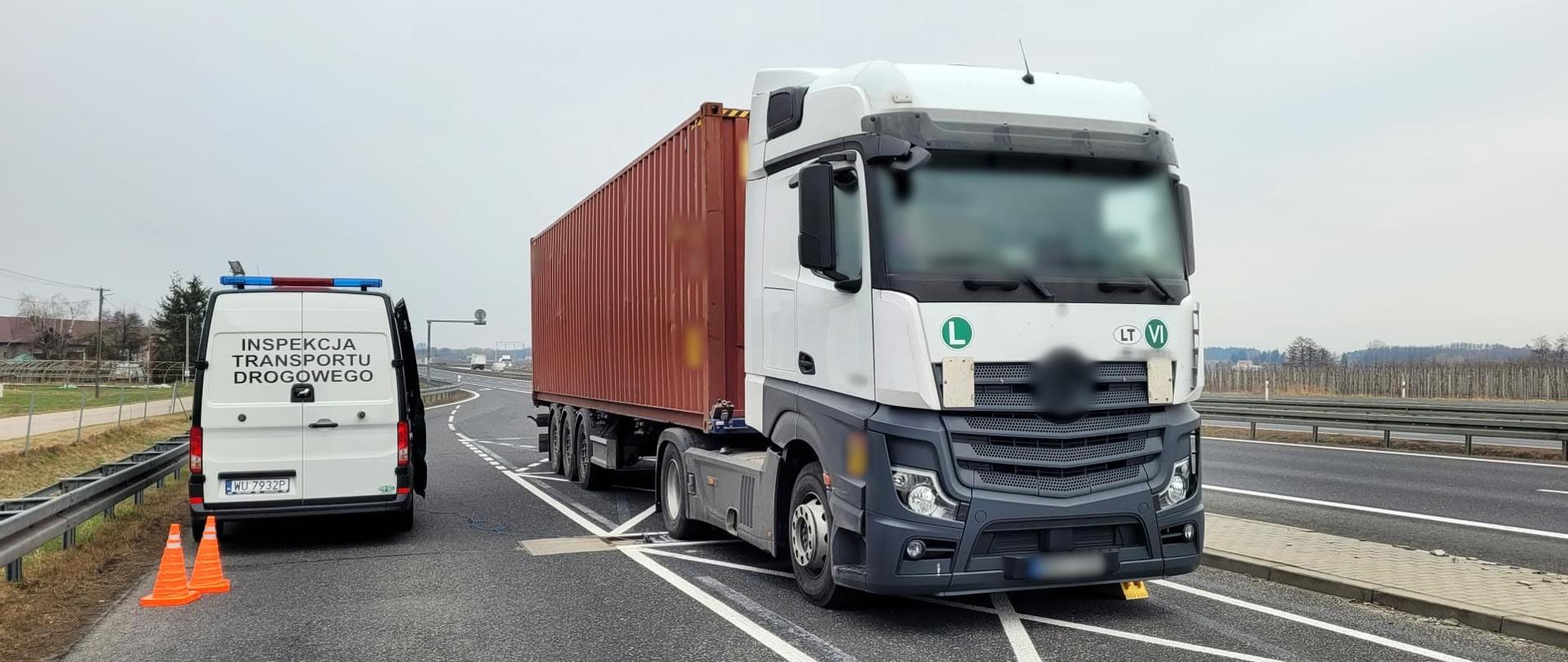 Od lewej: tył oznakowanego furgonu mazowieckiej Inspekcji Transportu Drogowego. Obok stoi na inspekcyjnych wagach ciągnik siodłowy z naczepą - kontenerem.