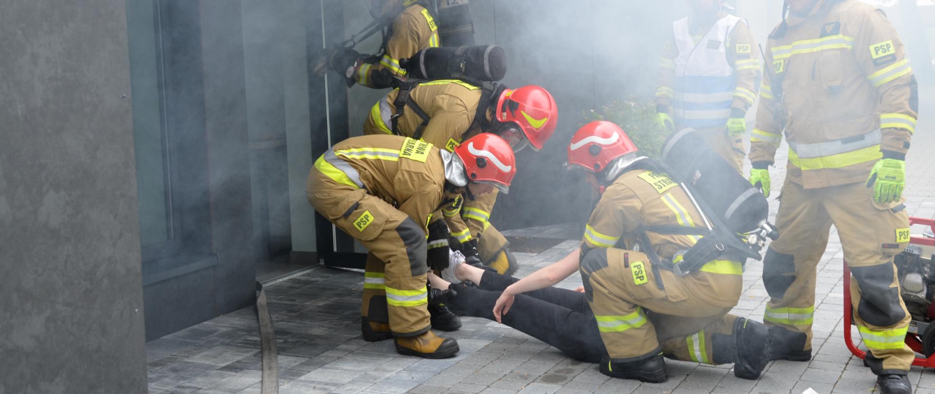 Strażacy ewakuują poszkodowaną osobę z zadymionego budynku.