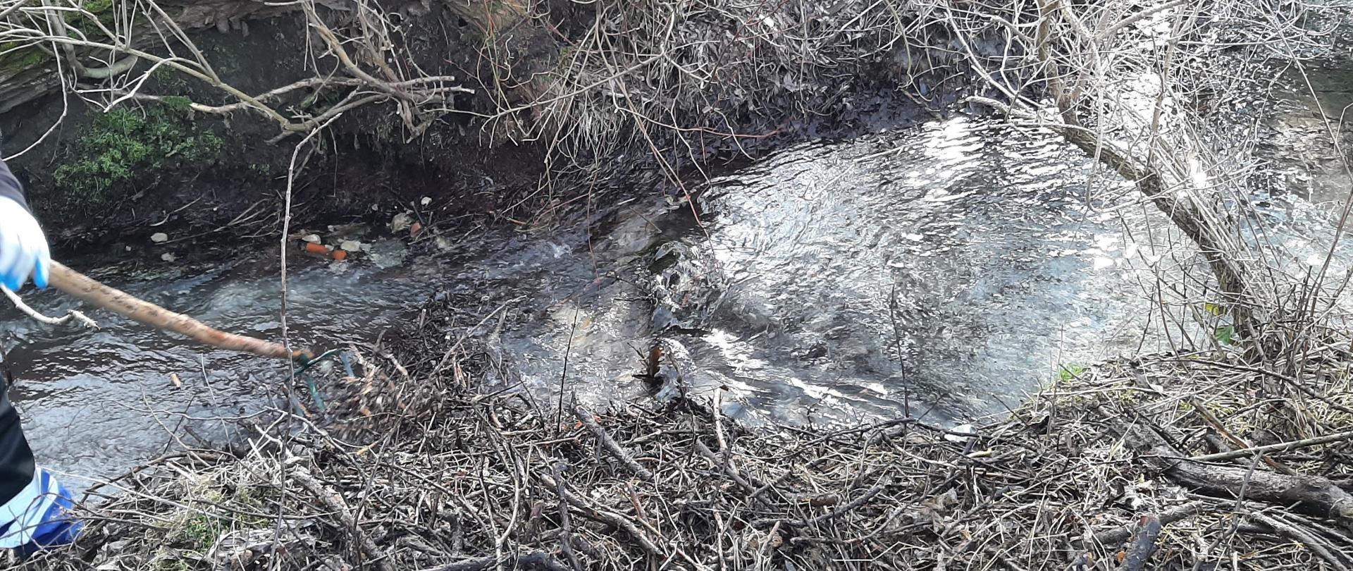 Rzeka. Z lewej strony widoczny fragment mężczyzny usuwającego zator.