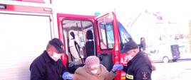 Pomoc przez strażaków Ochotniczej Straży Pożarnej w Trzcianie w wyjściu z pojazdu osobie starszej po dojeździe do punktu szczepień.