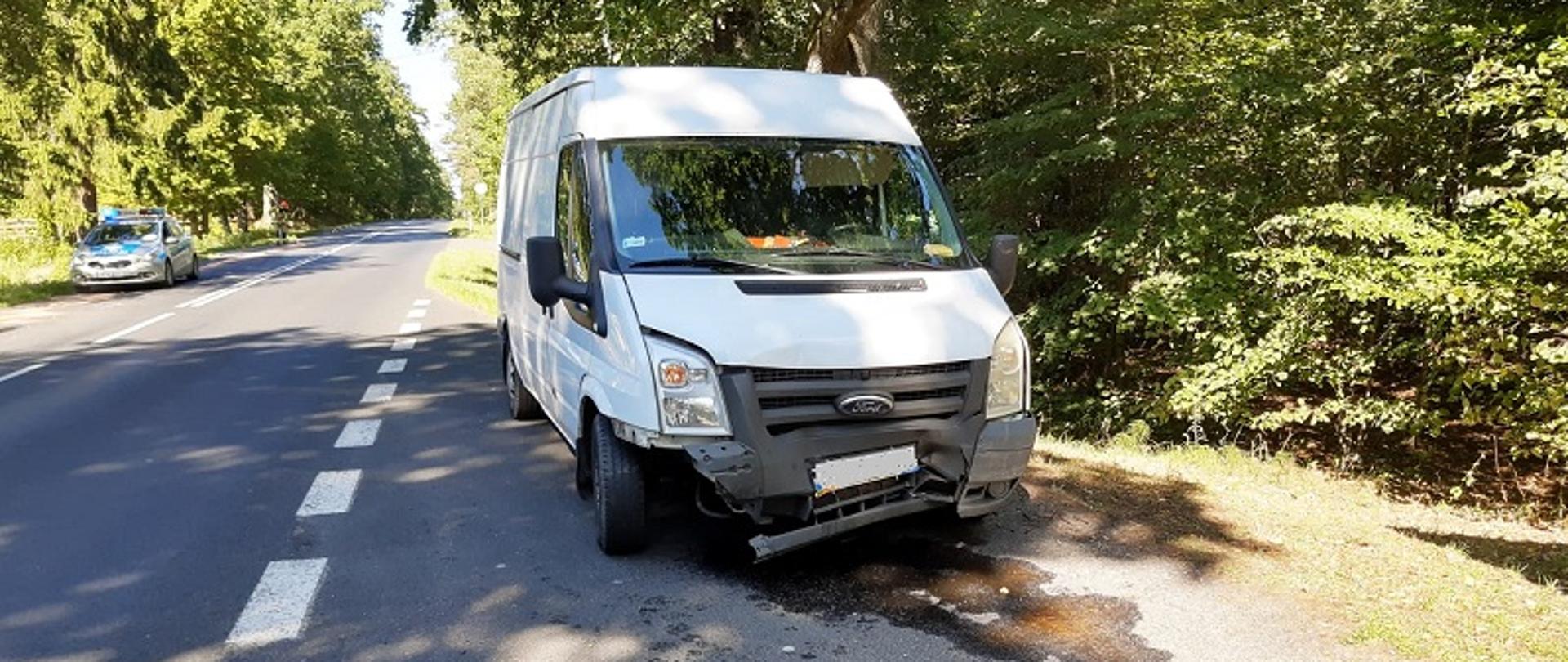 Kolizja w miejscowości Byszyno w powiecie białogardzkim. Zdjęcie przedstawia widoczny od przodu uczestniczący w zdarzeniu biały samochód dostawczy marki Ford z uszkodzonym płatem przednim maski. Na jezdni są widoczne wycieki płynów eksploatacyjnych. W głębi zdjęcia radiowóz policyjny