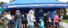 Na zdjęciu widoczna grupa dzieci i osób dorosłych uczestniczących w pikniku rodzinnym przed namiotem koloru niebieskiego z napisem Komenda Powiatowa PSP w Gorlicach pod którym strażacy prowadzili prelekcje i konkursy z zakresu bezpieczeństwa przeciwpożarowego.