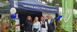 Cztery osoby, w tym kobieta w stroju ludowym, stoją przed namiotem Państwowej Inspekcji