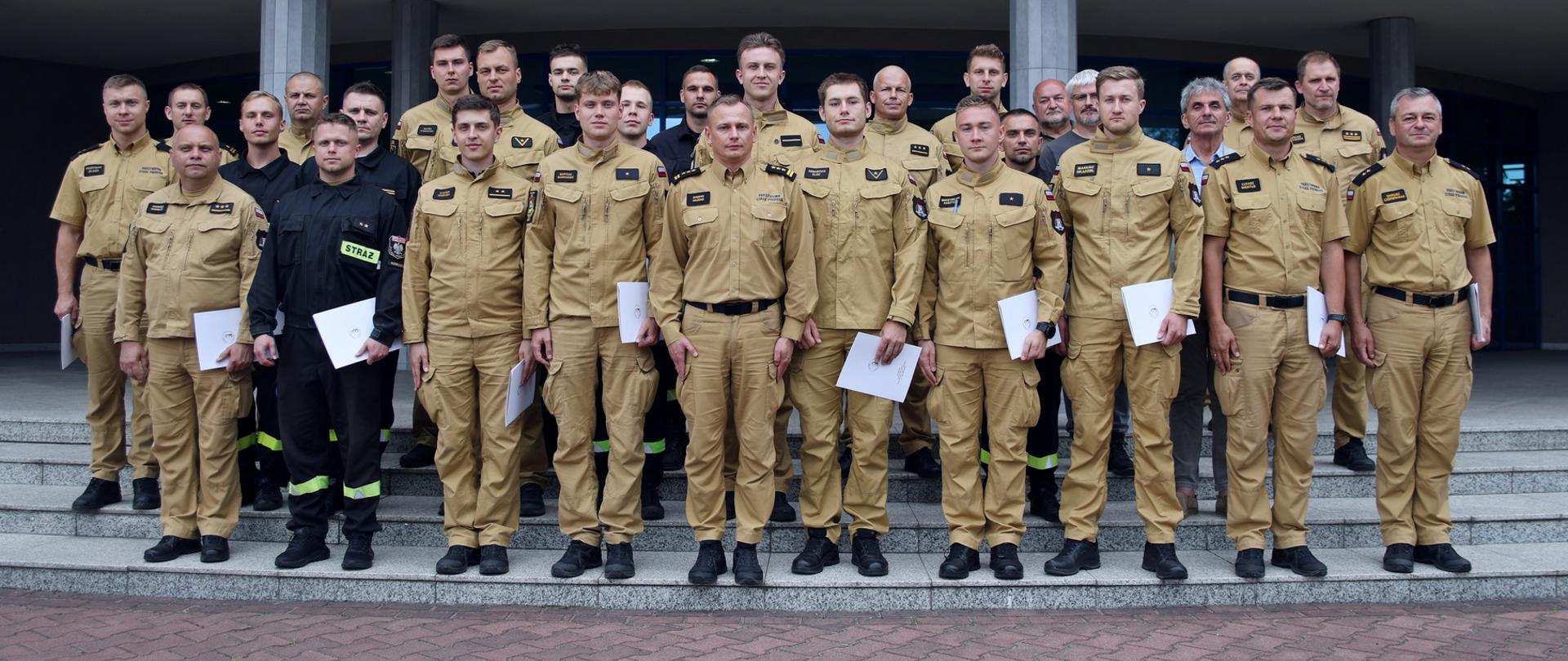 Pamiątkowe zdjęcie grupowe funkcjonariuszy PSP będących uczestnikami specjalistycznego szkolenia z zakresu awaryjnego rozładunku cystern (22 osoby) w towarzystwie Zastępcy Komendanta Centralnej Szkoły PSP, instruktorów podczas zajęć oraz trzech oficerów CS PSP