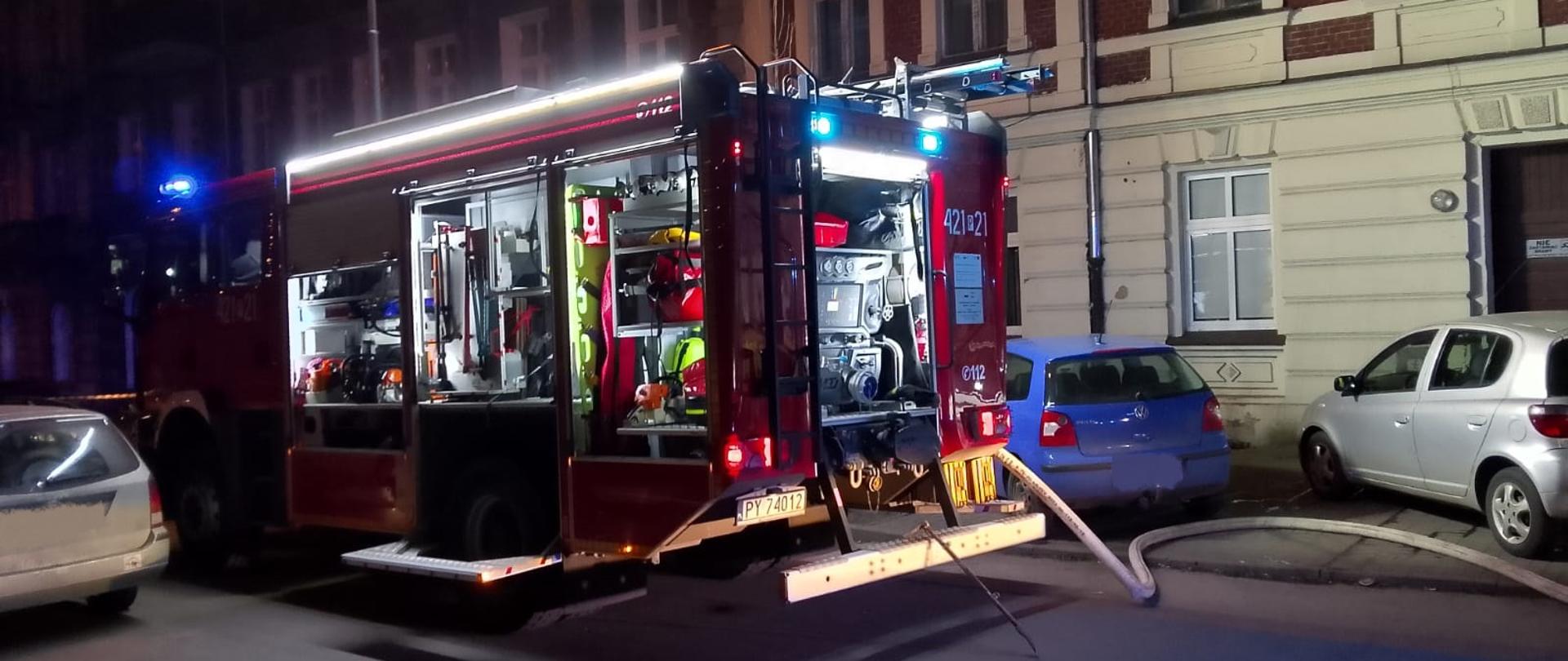 Na zdjęciu widać samochód pożarniczy, który ma pootwierane skrytki na sprzęt ratowniczy. Od samochodu pożarniczego rozwinięty jest wąż pożarniczy, przez który podawano wodę do celów gaśniczych. Jest pora nocna dlatego samochód pożarniczy oświetla teren działań.