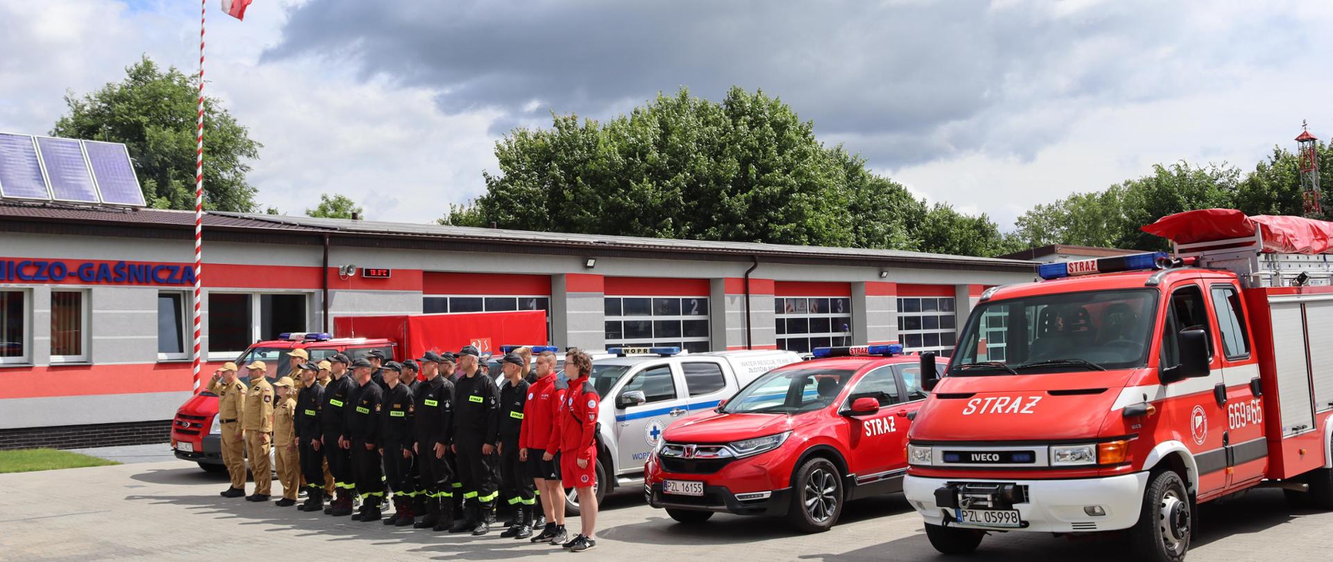 Strażacy stoją w szeregu w tle samochody strażackie