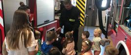 Zdjęcie przedstawia dzieci wraz z opiekunami przy samochodach strażackich, zapoznające się ze sprzętem pożarniczym. 