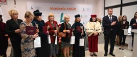 Na sali pod ścianą z napisem Akademia ANSiM stoi grupa osób trzymających czerwone teczki i małe papierowe torebki.