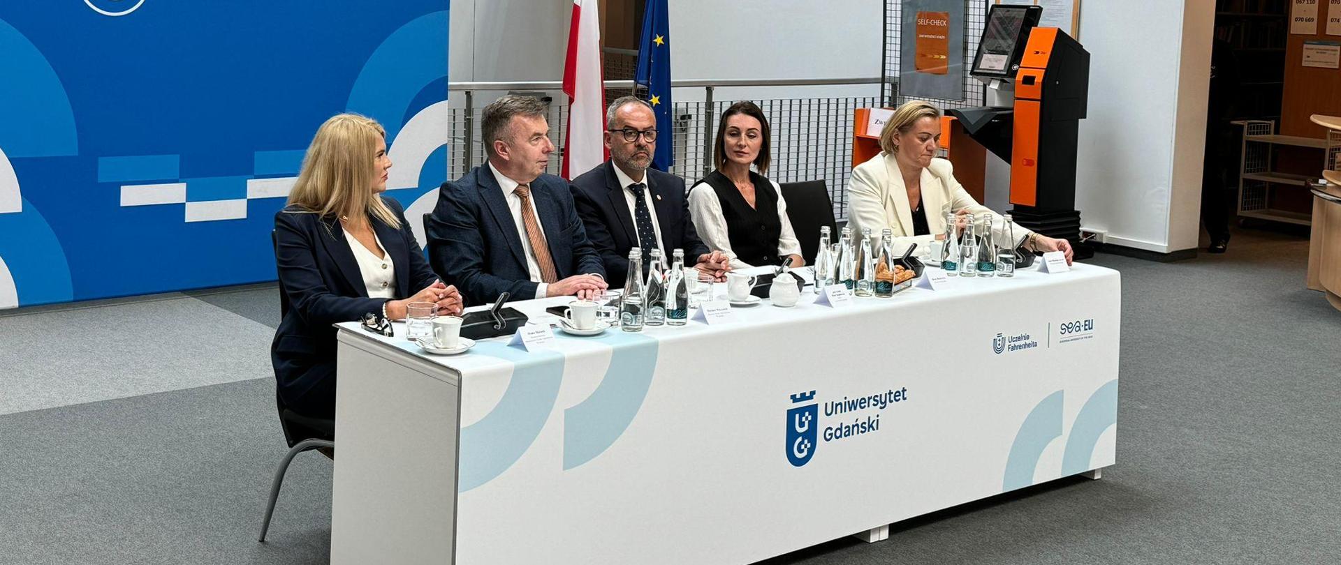 Za stołem prezydialnym siedzi kilka osób - 3 kobiety w tym wojewoda i wicewojewoda, a także dwóch mężczyzn - minister nauki i rektor uczelni