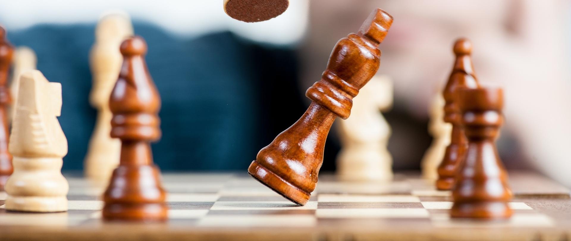 Szachownica wraz z pionkami. W tle rozmazany gracz szachista 