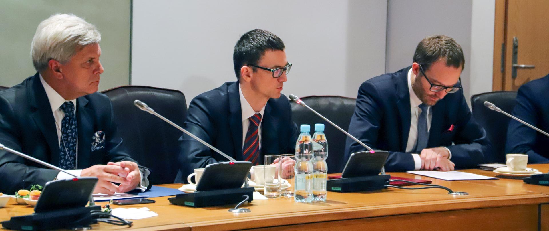 Trzech mężczyzn siedzi przy stole prezydialnym. Wśród nich wiceminister Karol Okoński.