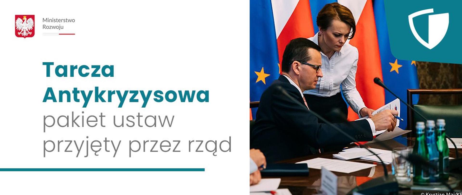 Po prawej stronie na zdjęciu premier Mateusz Morawiecki siedzi, obok stoi min. Jadwiga Emilewicz, spoglądają oboje na dokumenty