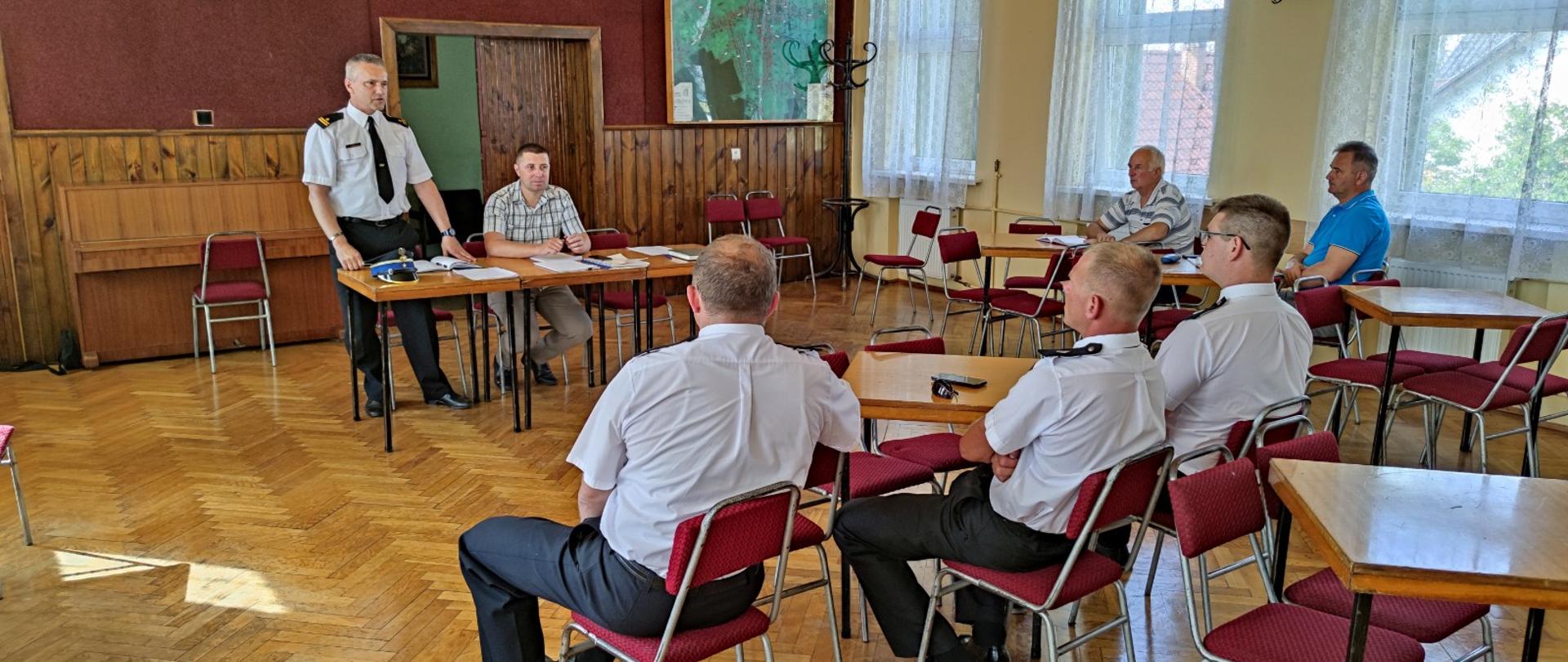 Sala, na sali strażacy, przemawia komendant