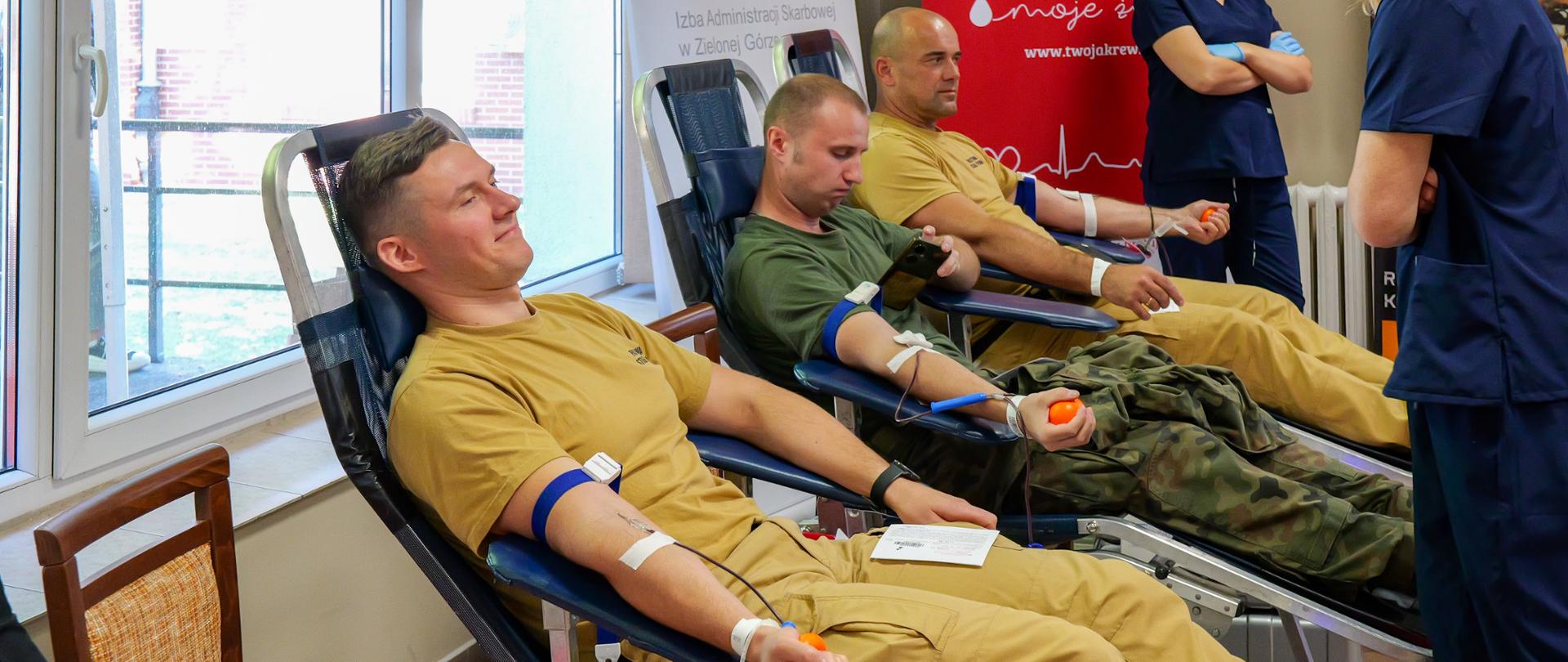 Kilku funkcjonariuszy różnych służb leży na fotelach i oddaje krew. Na rękach mają opaski uciskowe i przewody do poboru krwi.