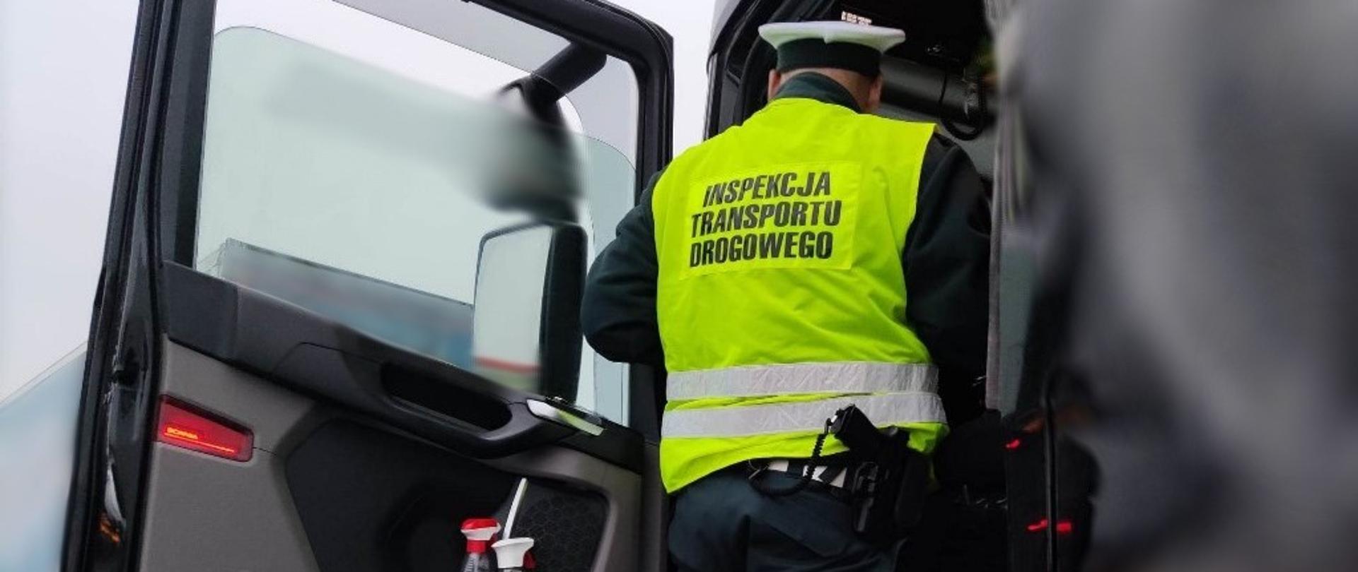 Umundurowany funkcjonariusze lubuskiej Inspekcji Transportu Drogowego stoi w wejściu do kabiny samochodu ciężarowego i pobiera dokumenty od kierowcy.