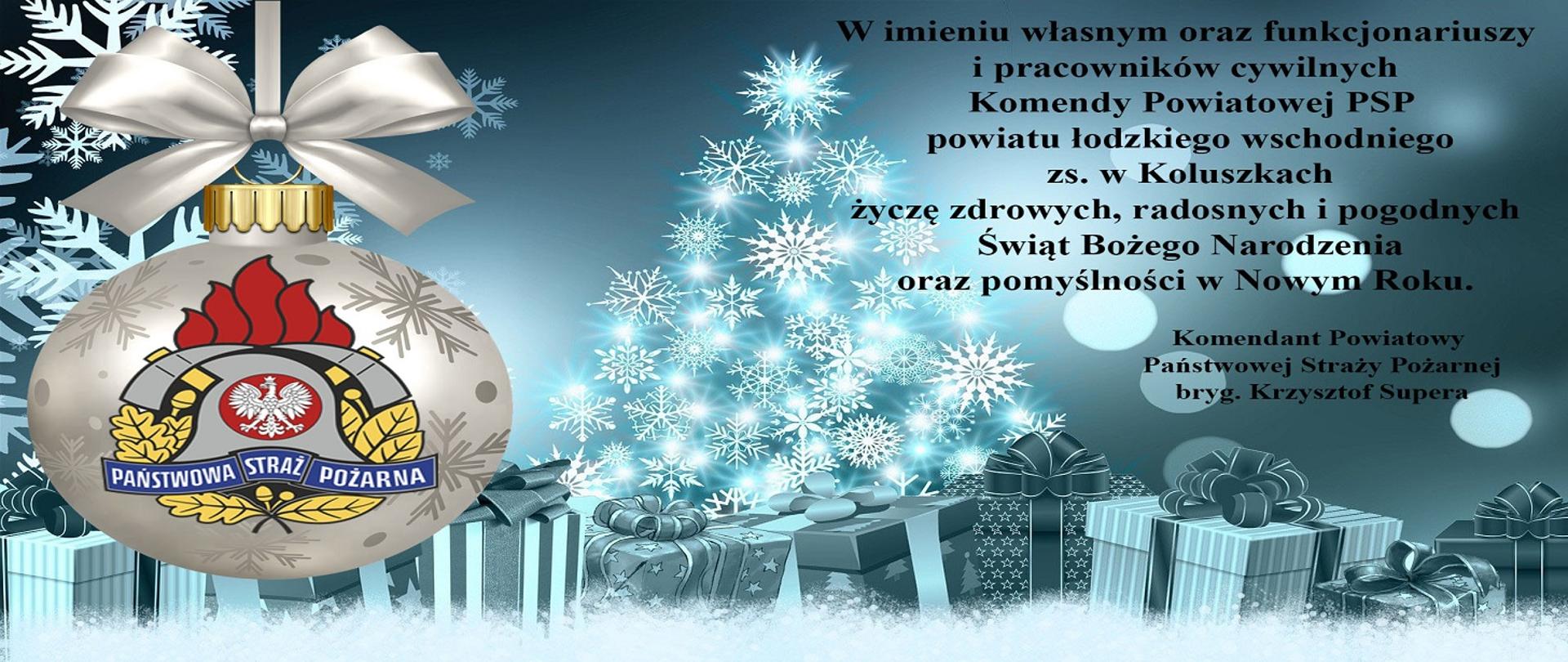 Zdjęcie przedstawia kartkę świąteczną a na niej życzenia; "W imieniu własnym oraz funkcjonariuszy i pracowników cywilnych Komendy Powiatowej PSP powiatu łódzkiego wschodniego zs. w Koluszkach życzę zdrowych, radosnych i pogodnych Świąt Bożego Narodzenia oraz pomyślności w Nowym Roku". Grafika przedstawia choinkę z płatów śniegu, pod nią prezenty, po lewej widoczna jest srebrna babka z logiem Państwowej Straży Pożarnej. 