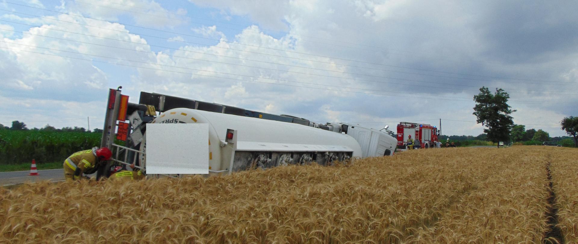 Na zdjęciu widać przewróconą cysternę znajdująca się na poboczu drogi przy polu ze zbożem.