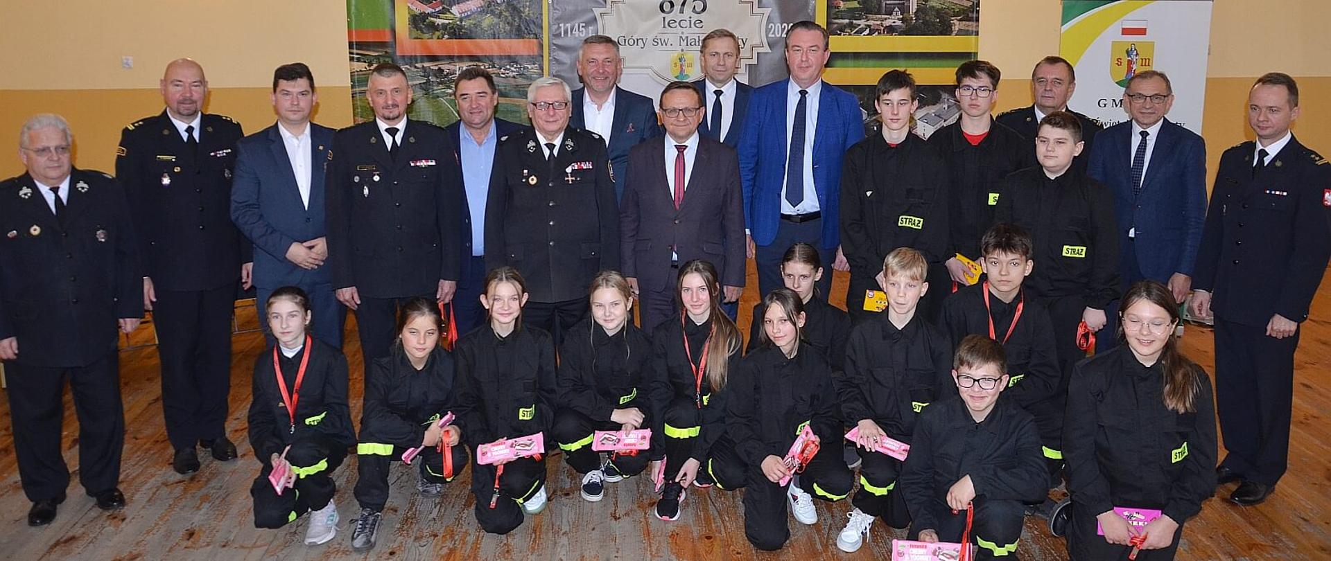 uczestnicy uroczystości wręczenia promes dla młodzieżowych drużyn pożarniczych pozują do zdjęcia zbiorowego wśród nich młodzież mdp, strażacy druhowie, posłowie i senatorowie RP, przedstawiciele władz samorządowych