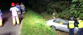 Strażacy zabezpieczają miejsce zdarzenia po wypadku. W rowie stoi rozbity samochód osobowy. 