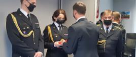 Zdjęcie przedstawia wręczenie przez Komendanta Miejskiego PSP w Białymstoku drobnych upominków okolicznościowych