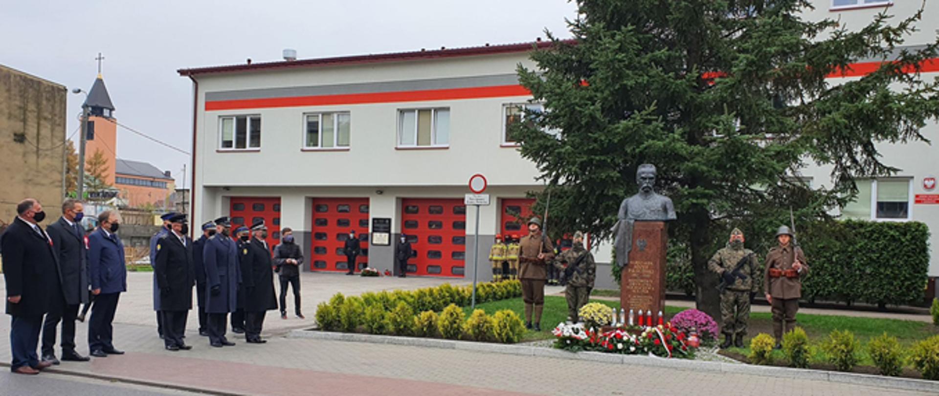 Delegacja przedstawicieli samorządów i służb przygotowuje się do złożenia wiązanek kwiatów pod popiersiem marszałka Józefa Piłsudskiego, przed Komendą Powiatową PSP w Sochaczewie.