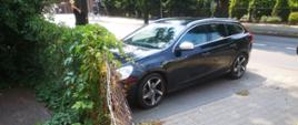 Widać czarny samochód na parkingu, jest blisko ogrodzenia posesji