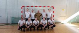 Drużyna KP PSP Sokołów Podlaski wraz z komendantem KP PSP w Przasnyszu. Zdjęcie zrobiona na hali gimnastycznej w tle bramka do futsalu wraz z siatką.
