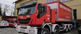 Samochód ciężarowy KP PSP w Oświęcimiu w kolorze czerwonym stoi tyłem do garażu Jednostki Ratowniczo-Gaśniczej w Wadowicach w trakcie rozładunku maseczek ochronnych. 