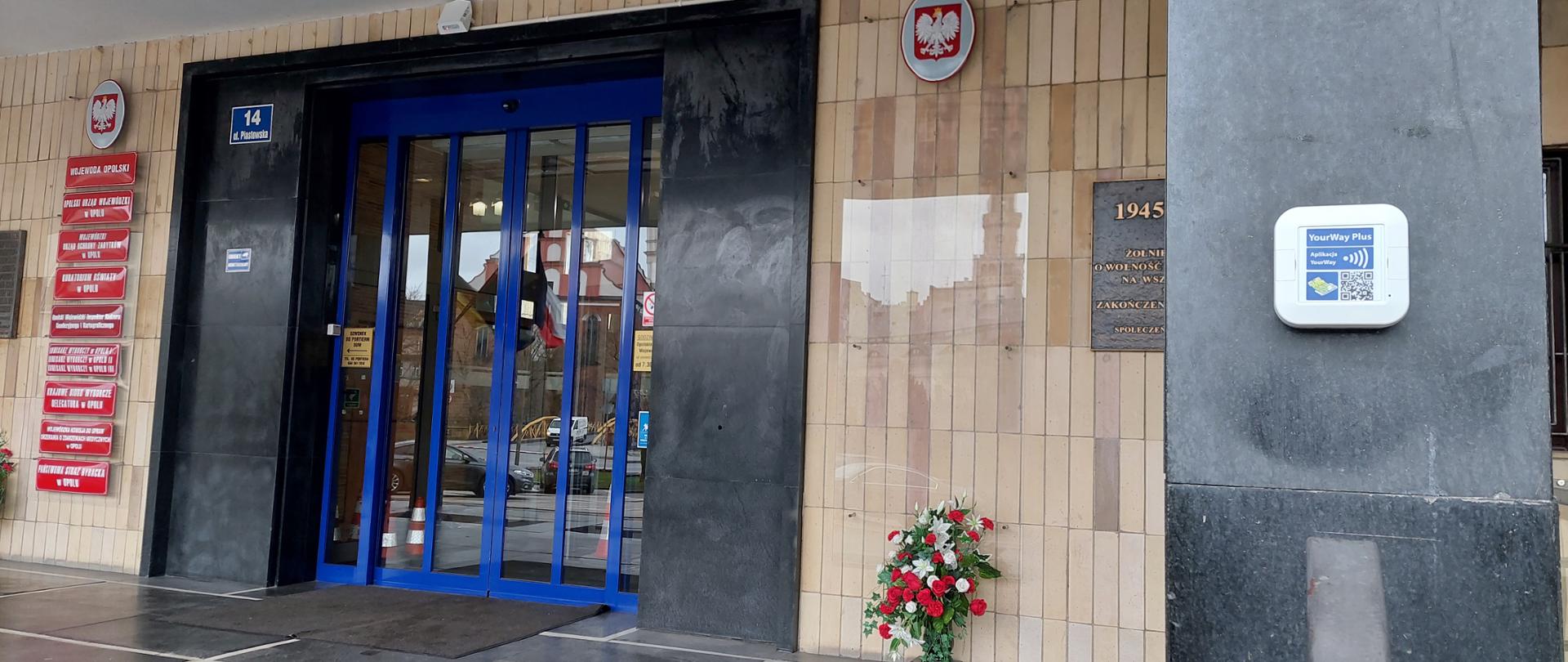 Na zdjęciu znajduje się wejście główne do budynku Opolskiego Urzędu Wojewódzkiego oraz zainstalowany obok nadajnik YourWay. YourWay jest to system wspierający osoby niewidome oraz słabowidzące w łatwiejszym poruszaniu się w przestrzeni publicznej. 